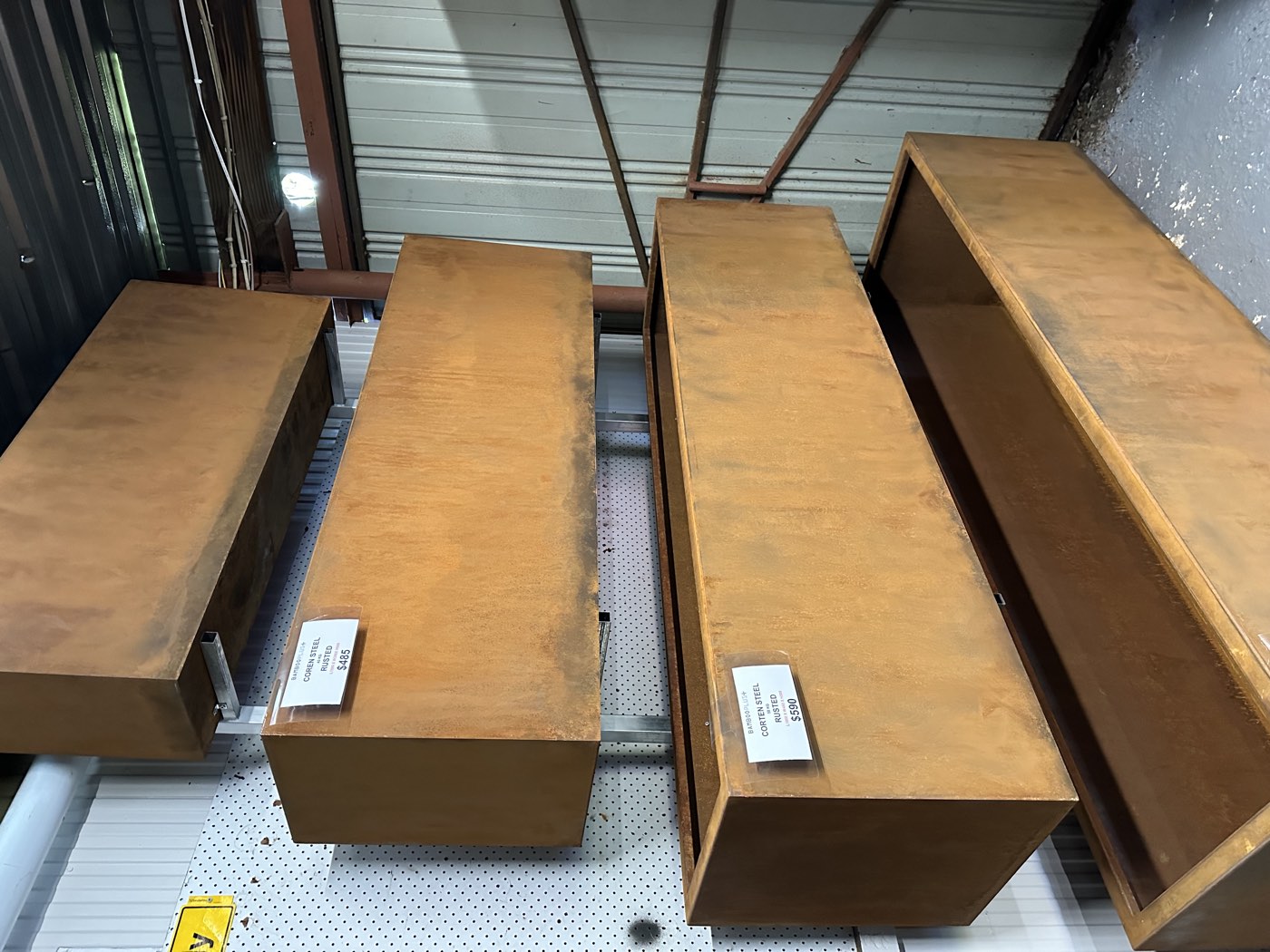 Corten planters in the supplier's showroom with price tags attached, showing several of the standard rectangular sizes.