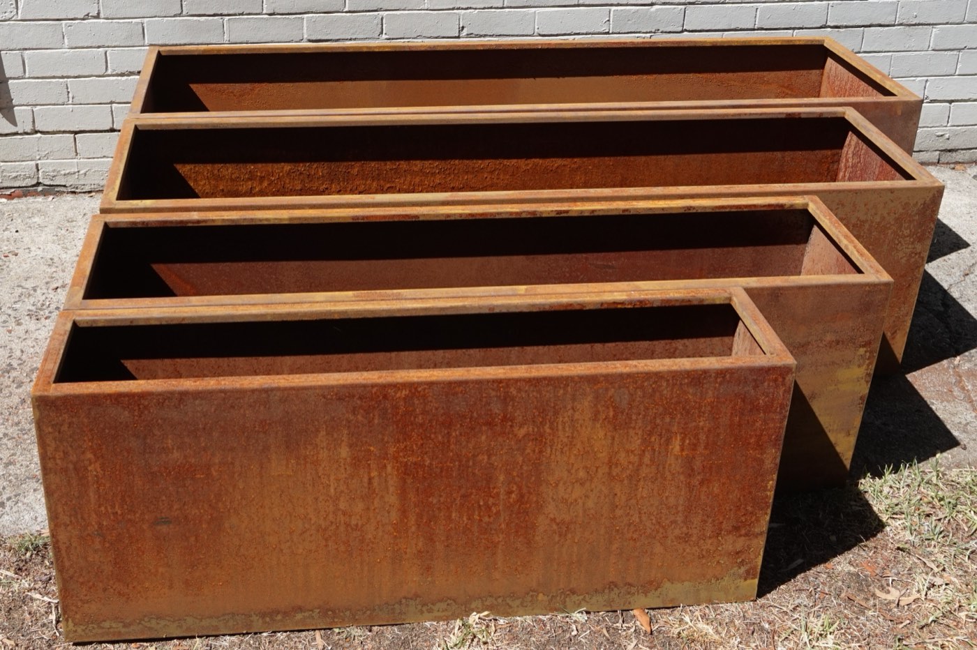The same four rectangular corten planters empty and nested, showing the range of lengths and the folded top edge.